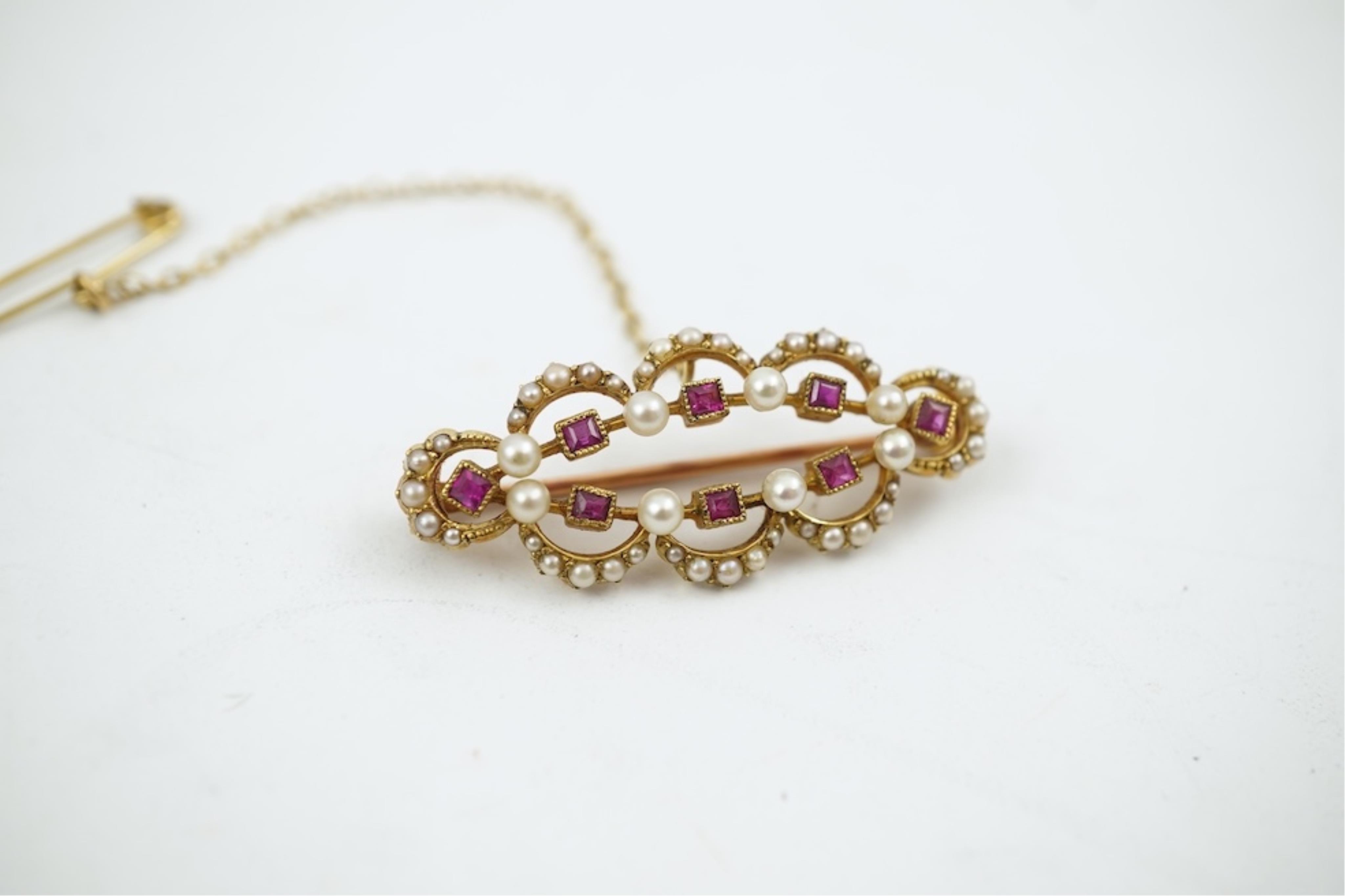 An Edwardian 15ct, ruby and seed pearl cluster set brooch, 33mm, with safety chain, gross weight 4.1 grams.